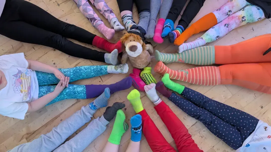 Kinderbeine mit bunten Socken im Kreis um ein Plüsch-Löwen