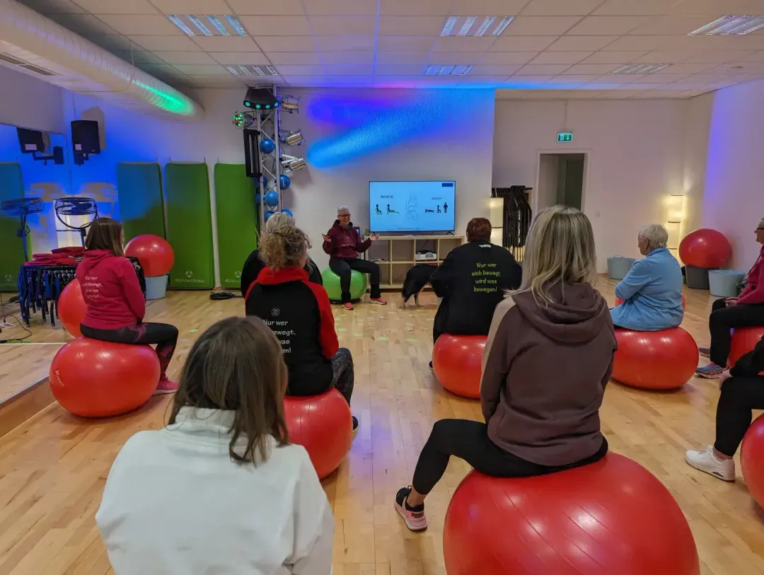 Kleine Gruppe sitzt auf Gymnastikbällen im Kursraum